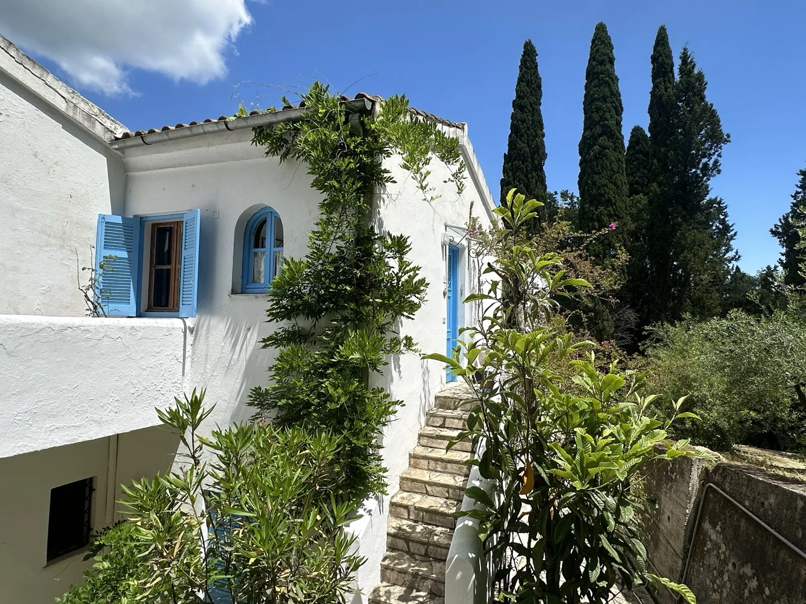 Whitewashed house with blue shutters and stone steps in Gouvia, Corfu